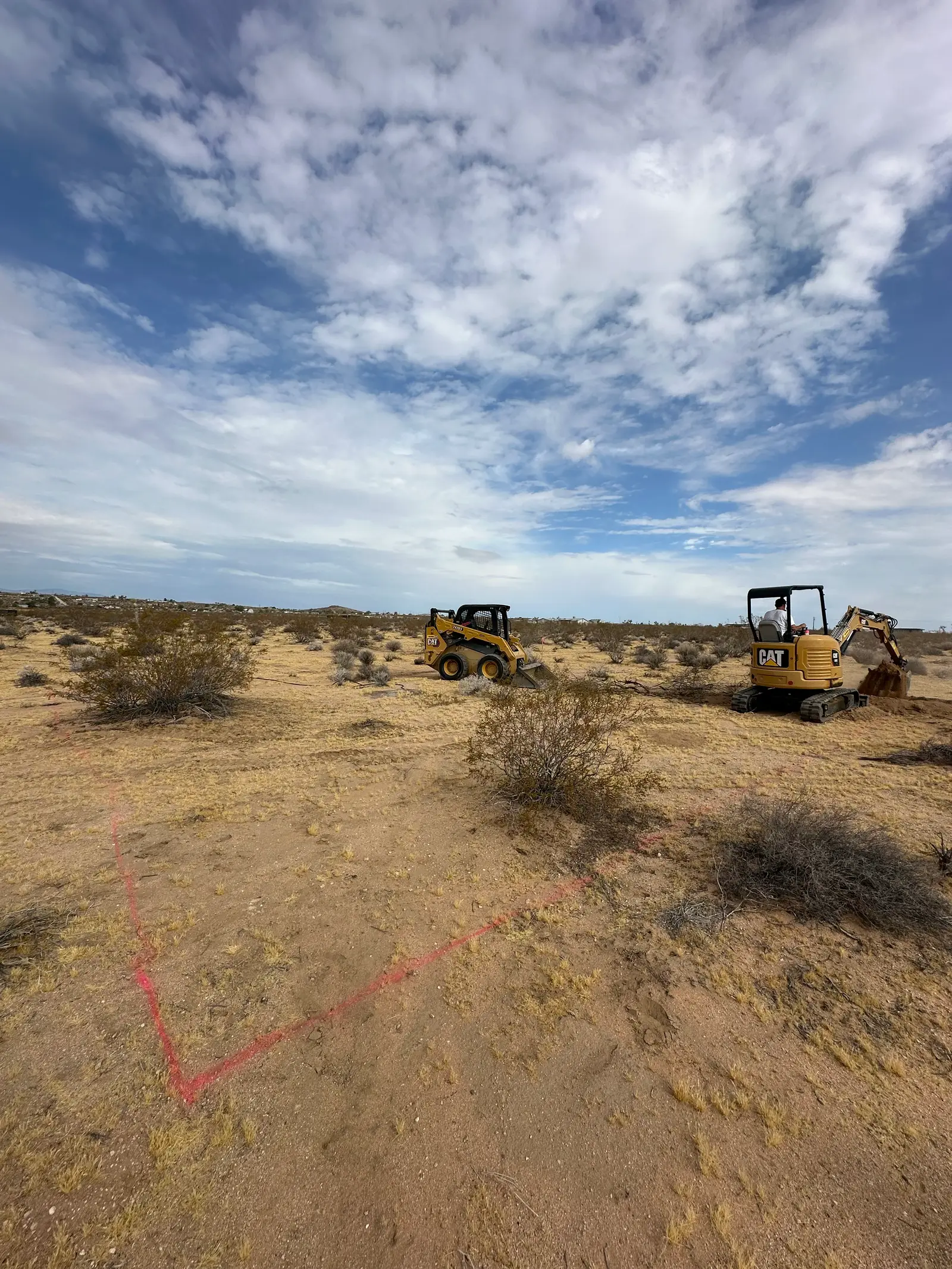 Orange survey paint and wooden stakes marking the house footprint on undisturbed desert ground.