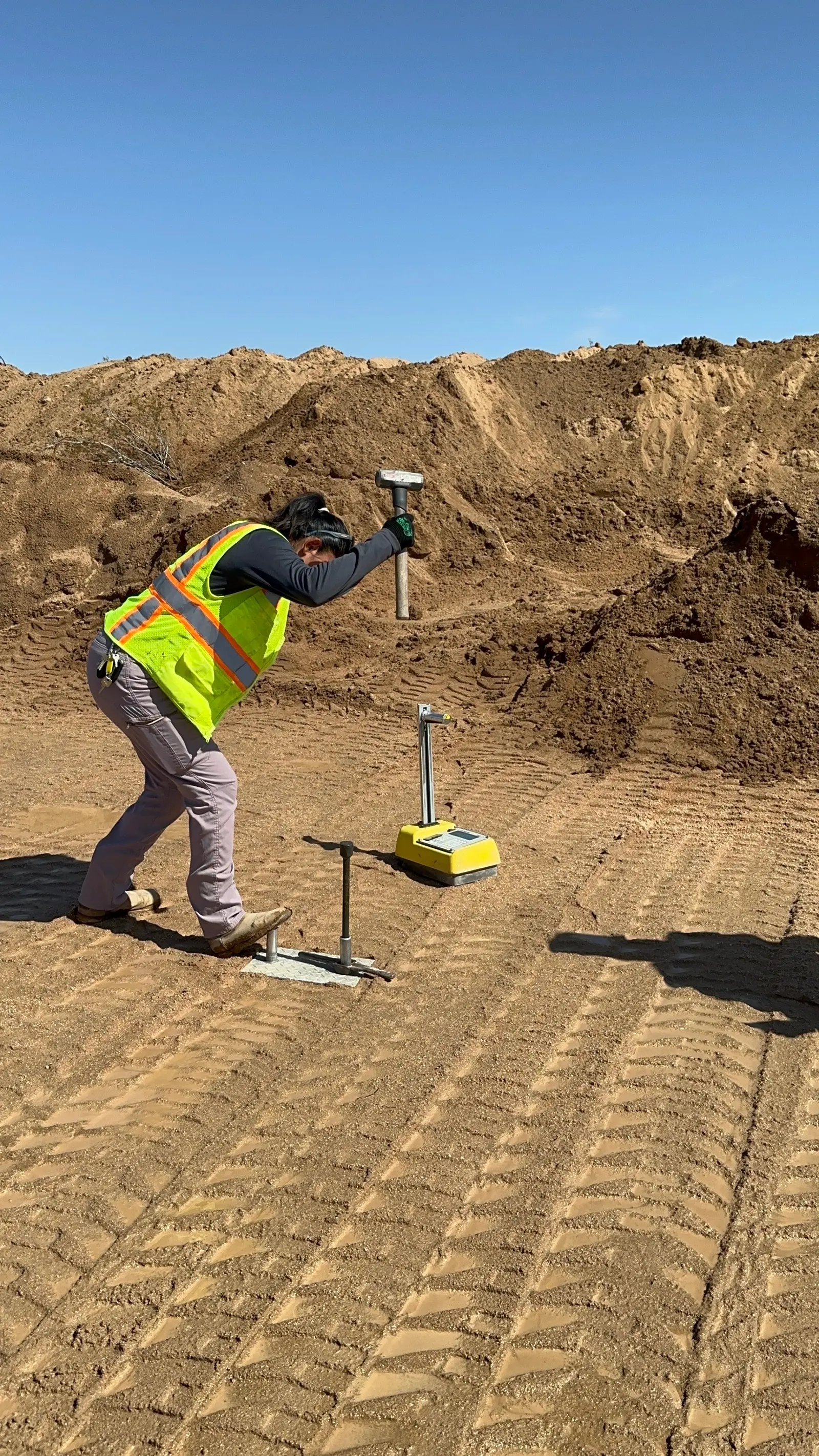 A worker driving a test hammer into the graded pad during a soil compaction test.